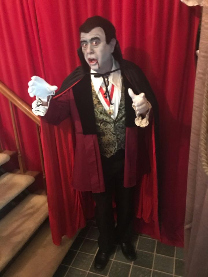 A man in a vampire costume is standing in front of a red curtain.