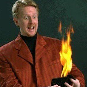 A man in a red jacket is holding a wallet with flames coming out of it.