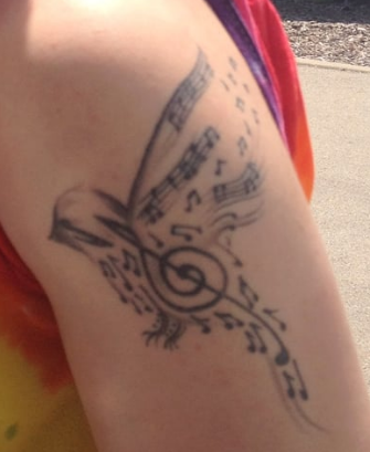 A person has a tattoo of a bird and music notes on their arm
