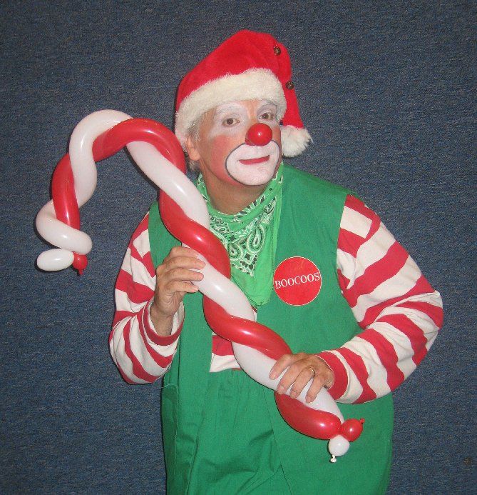 A clown in a santa hat is holding a candy cane made of balloons