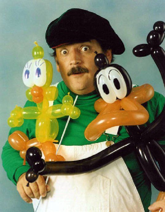 A man in a green shirt is holding balloons in the shape of animals