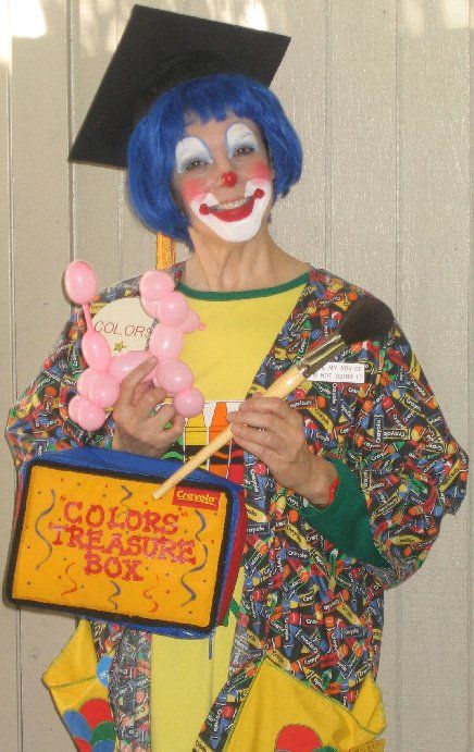 A clown wearing a graduation cap is holding balloons and a box that says colors treasure box