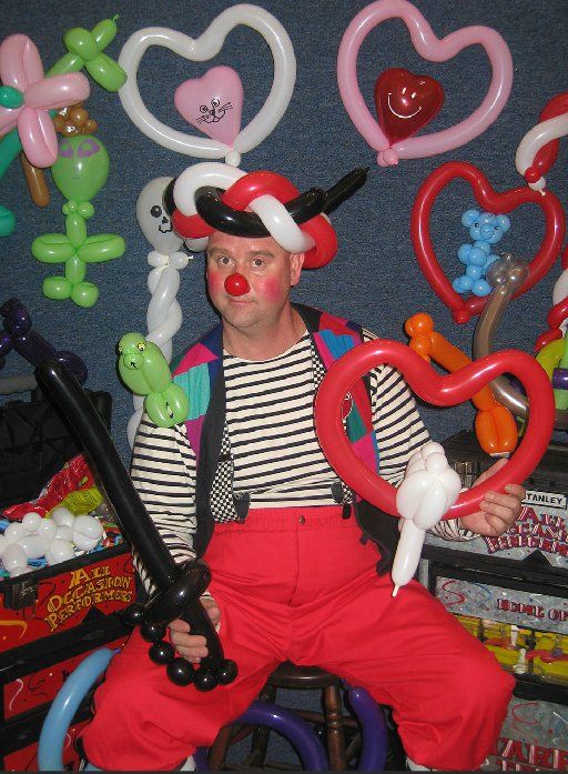 A man in a clown costume is holding a heart shaped balloon
