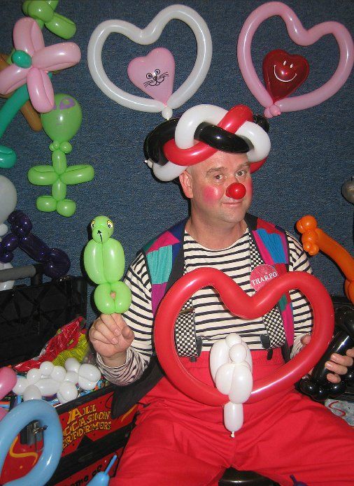 A clown is holding a heart shaped balloon