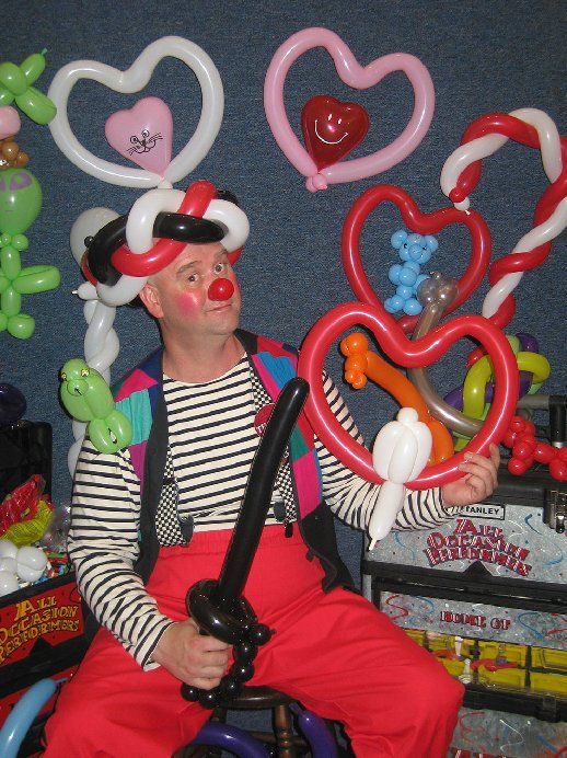 A clown is holding balloons in the shape of hearts