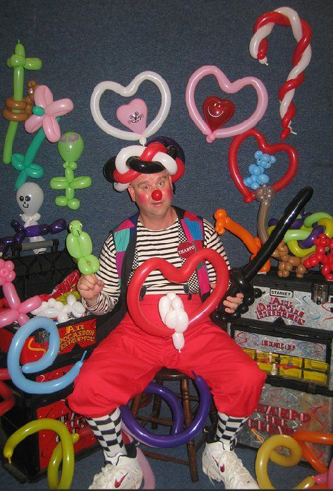A clown is sitting on a chair surrounded by balloons