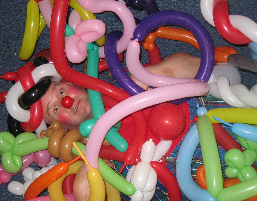 A clown is laying in a pile of balloons