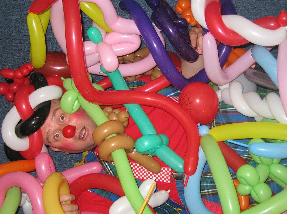 A clown is laying in a pile of balloons