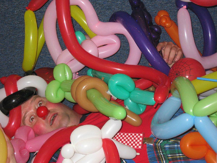 A clown is laying in a pile of balloons