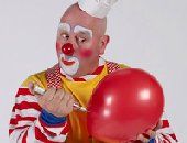 A clown is blowing up a red balloon with a pen.