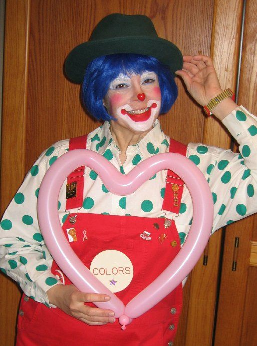 A woman dressed as a clown is holding a pink heart shaped balloon