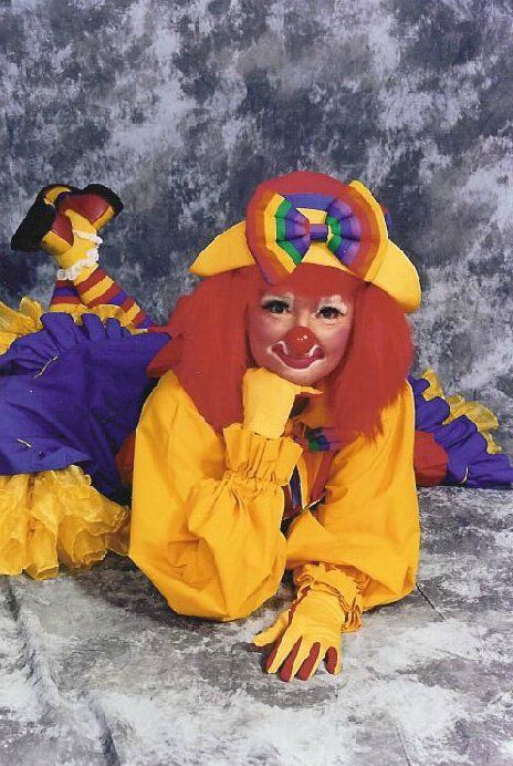 A clown in a yellow and purple outfit is laying on the floor