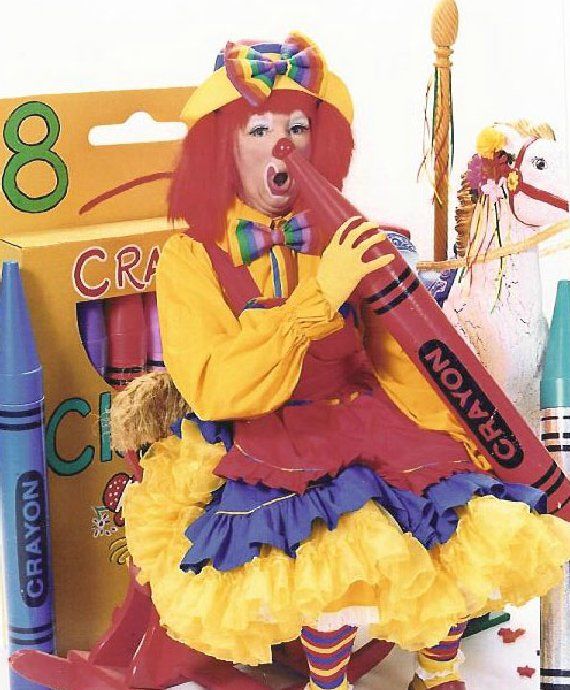 A clown is holding a red crayon in front of a box of crayons