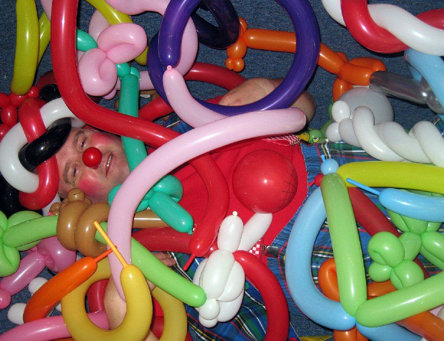 A clown is laying in a pile of balloons