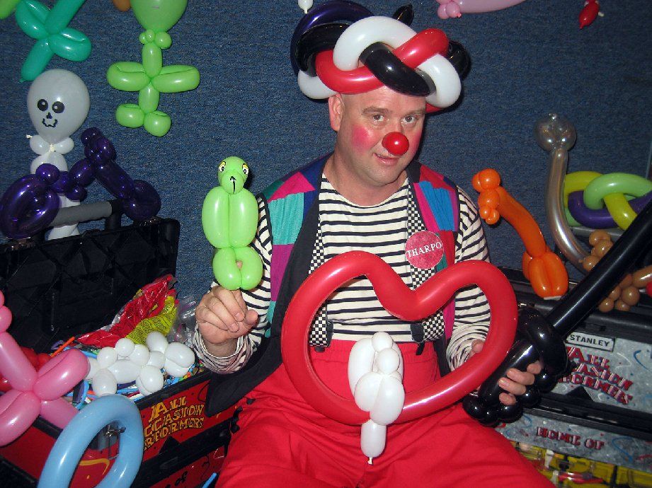A man dressed as a clown is holding a heart shaped balloon