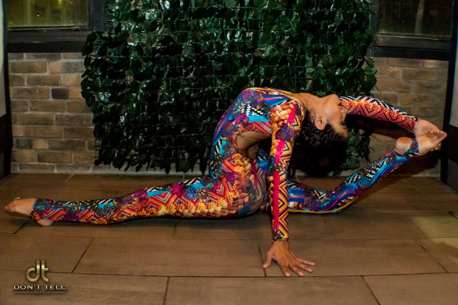 A woman in a colorful jumpsuit is doing a split on the floor.