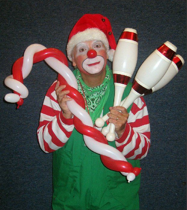 A clown in a santa hat is holding candy canes and juggling pins