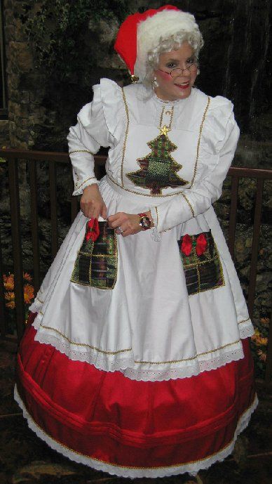 A woman in a santa claus costume is standing in front of a fence.