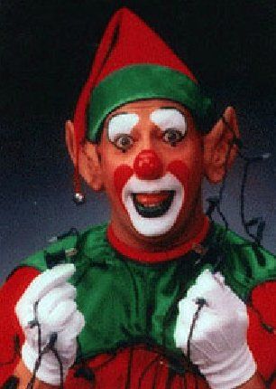 A clown dressed as an elf is holding christmas lights