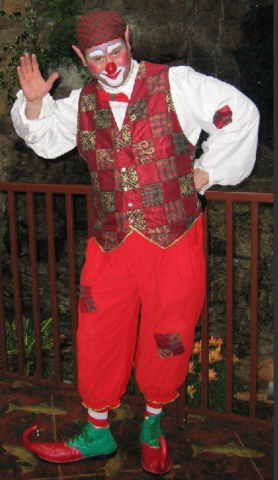 A man dressed as a clown is standing in front of a railing