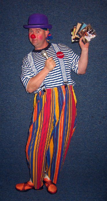 A man dressed as a clown is holding a microphone and playing cards