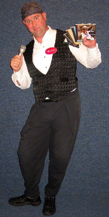 A man in a tuxedo is holding a microphone and a fan