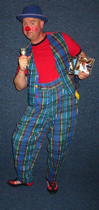 A man dressed as a clown is holding a microphone and a book.