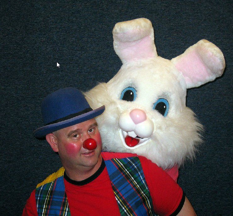 A clown with a red nose is standing next to a stuffed bunny