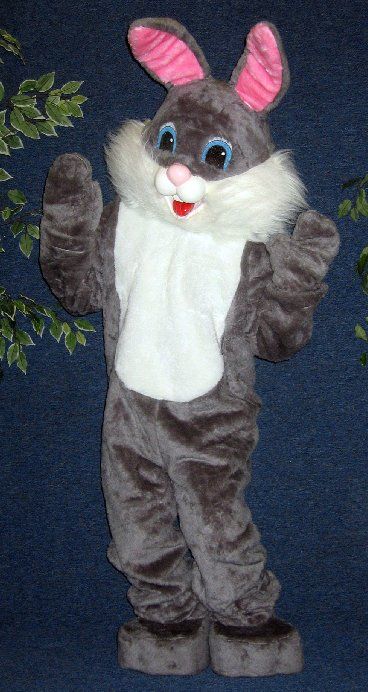 A gray and white bunny mascot is standing in front of a tree.
