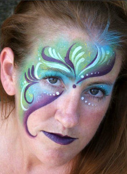 A woman has her face painted with a purple and green design