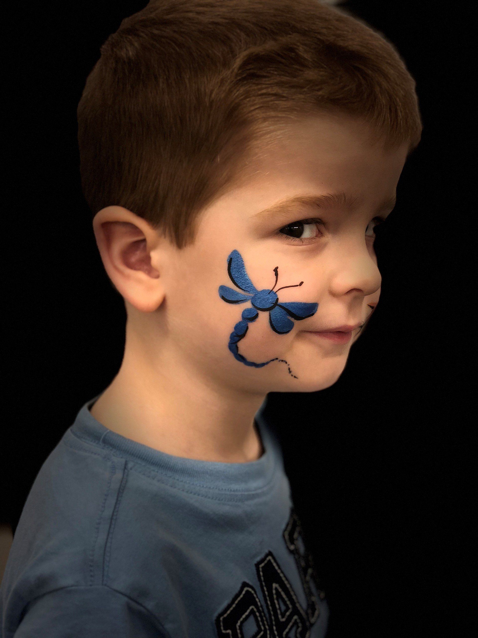 A young boy has a dragonfly painted on his face