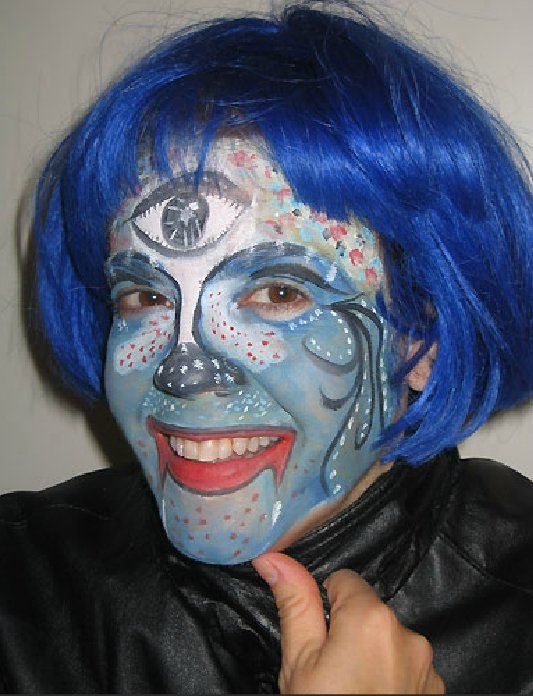 A woman with blue hair has her face painted with a third eye