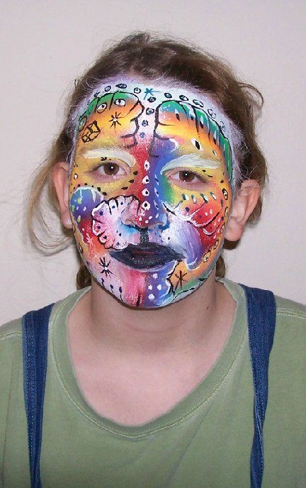 A young girl has her face painted in a colorful design.