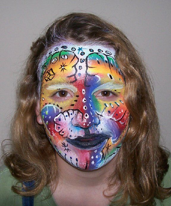 A young girl has her face painted in a rainbow of colors