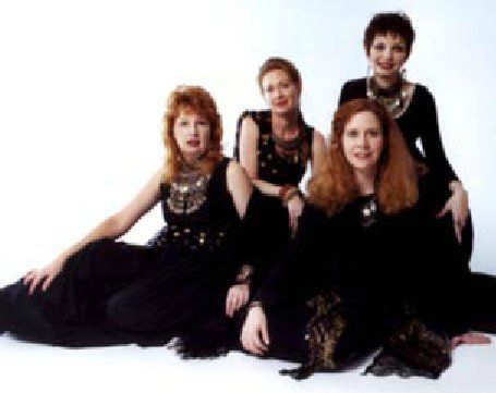Four women in black dresses are posing for a picture