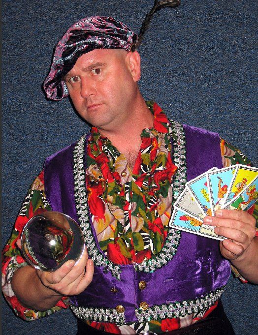 A man in a purple vest is holding tarot cards and a crystal ball
