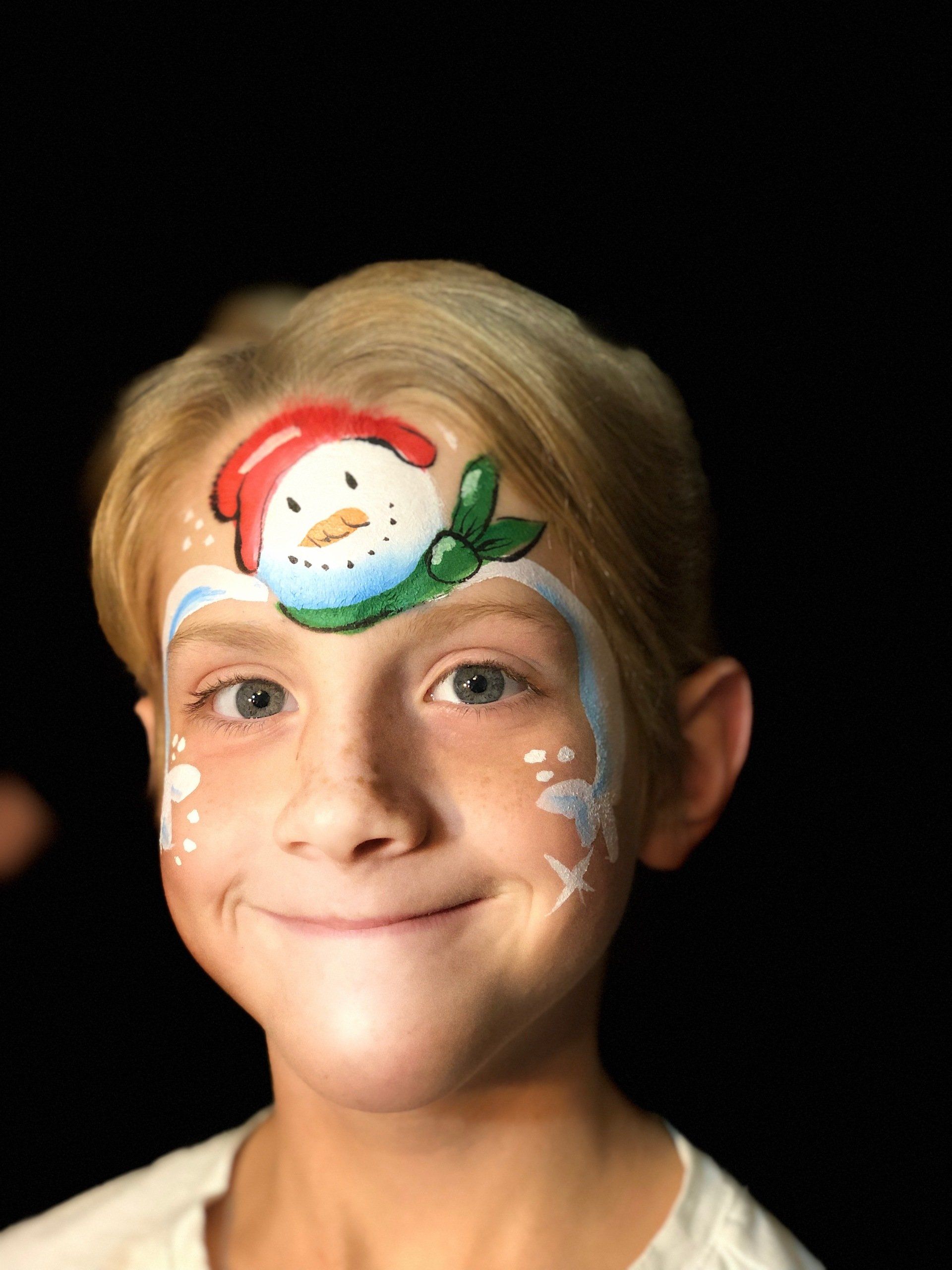 A little girl has a snowman painted on her face.