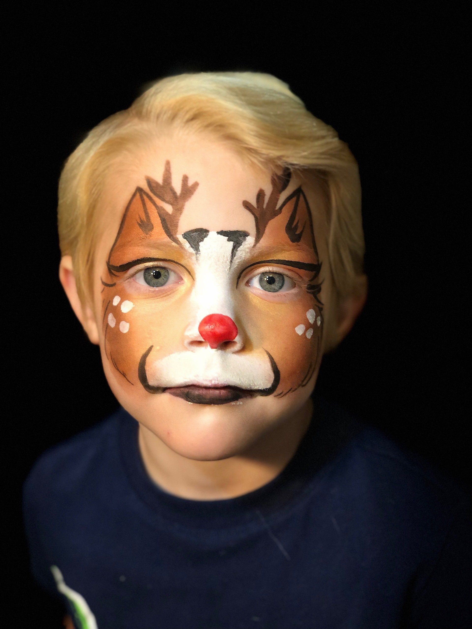 A young boy with his face painted like a reindeer.