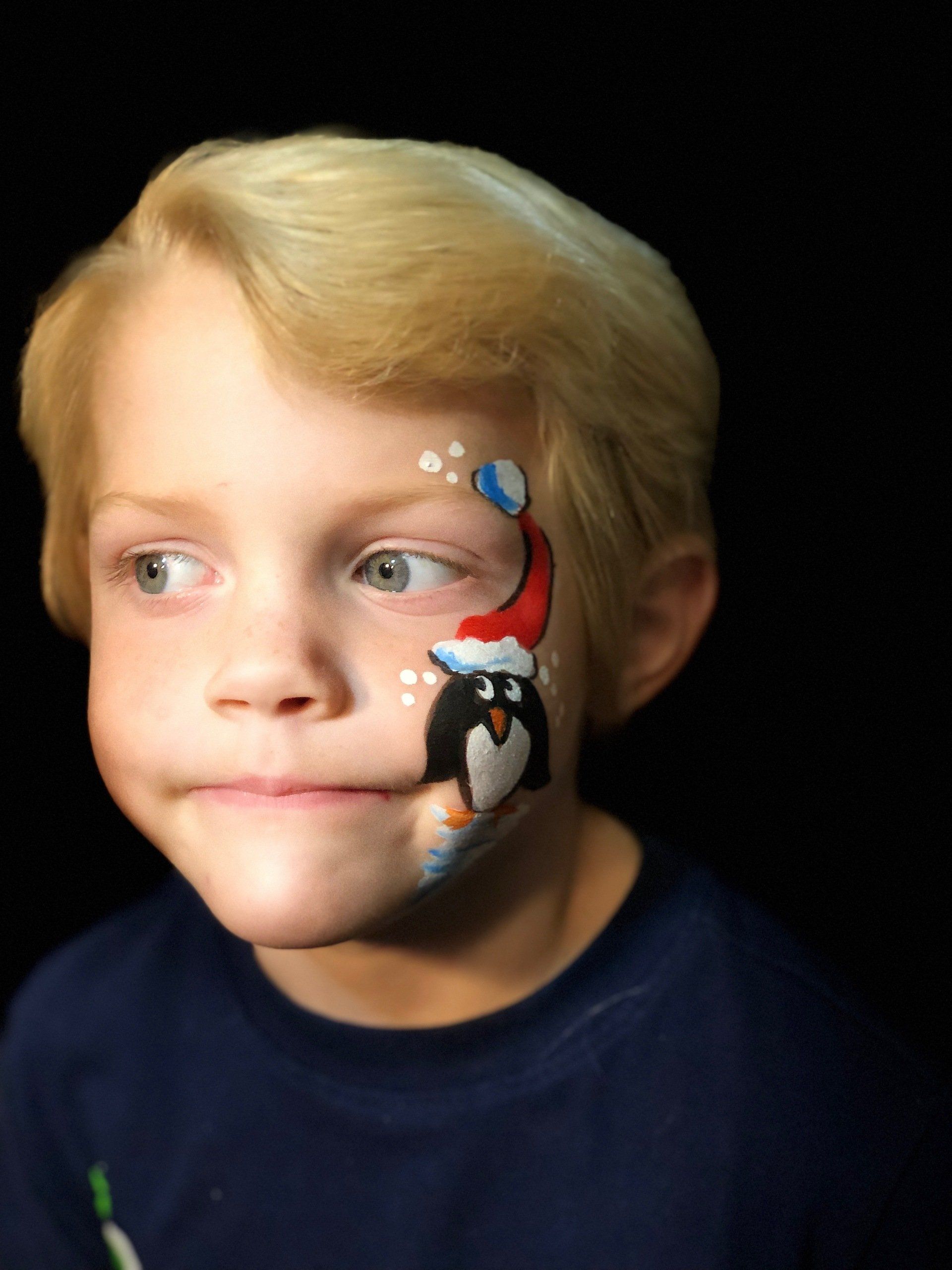 A young boy has a penguin painted on his face.