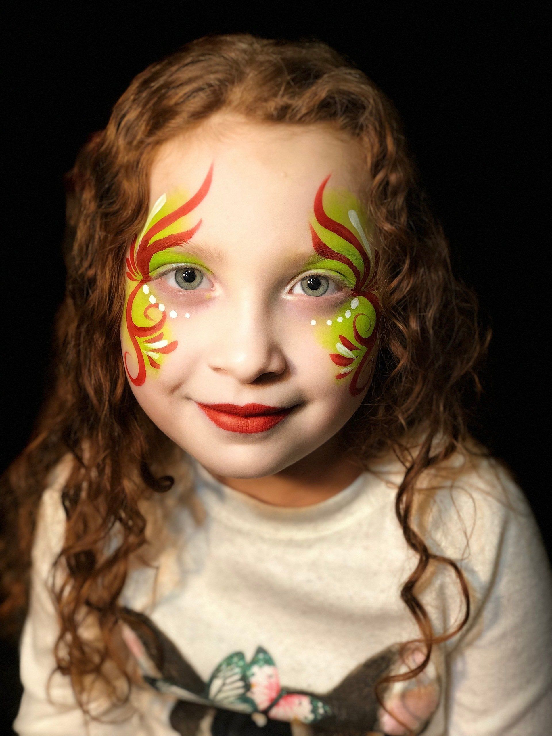 A little girl with her face painted has a butterfly on her shirt.