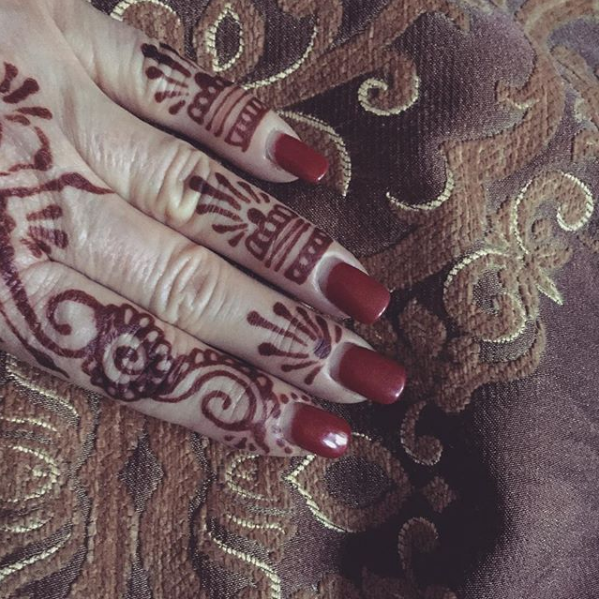A close up of a woman 's hand with henna and red nails