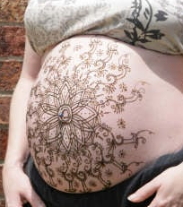 A pregnant woman has a henna tattoo on her belly.