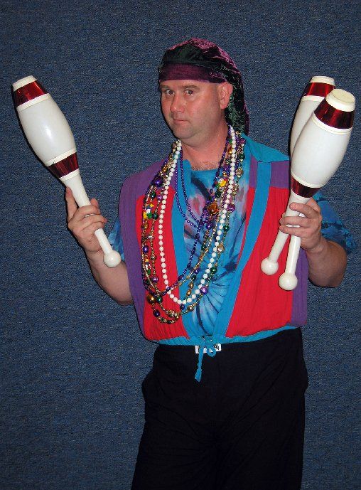 A man in a mardi gras outfit is holding two juggling pins