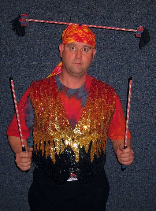 A man wearing a bandana and a vest is holding two sticks
