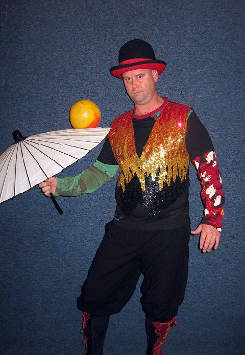 A man in a clown costume is balancing a ball on an umbrella
