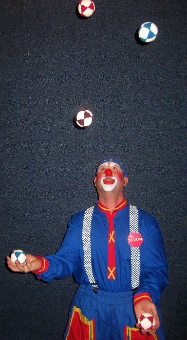 A clown juggling three balls in front of a black background