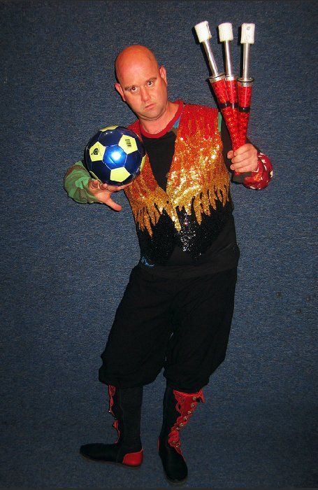 A bald man is holding a soccer ball and juggling sticks
