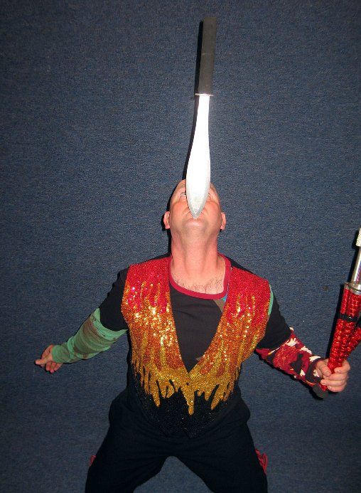 A man in a colorful costume is juggling a stick with his mouth