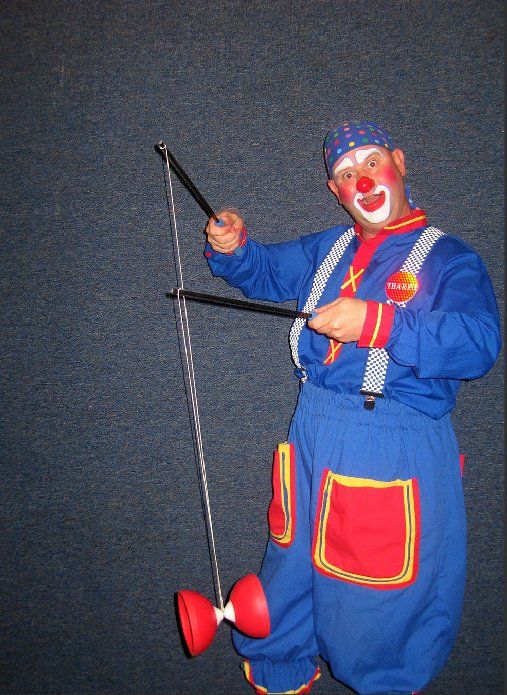 A clown in a blue outfit is juggling a pair of diabolos