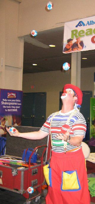 A clown is juggling balls in front of a sign that says read